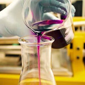 Lab chemicals being poured from one beaker to another beaker.
